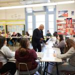 Teacher speaks with a student seated in a ring of desks